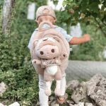 Kleinkind trägt einen personalisierten Teddy-Rucksack mit einer abnehmbaren Stoffpuppe und dem Namen "Maks", im Freien unterwegs.