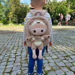 Kind mit einem personalisierten Teddy-Rucksack und dem Namen "Konrad", spaziert auf einem gepflasterten Weg im Park.