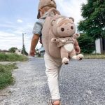 Kleinkind mit einem personalisierten Teddy-Rucksack und dem Namen "Maks", spaziert auf einer ländlichen Straße bei sonnigem Wetter.